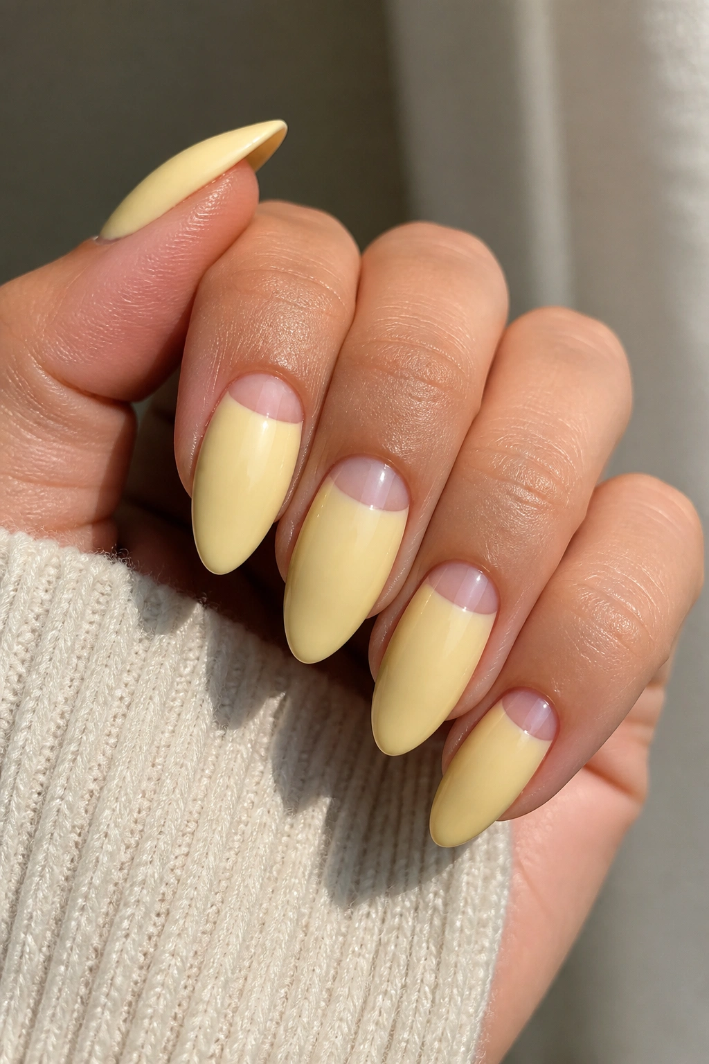 Almond nails featuring half-moon negative space at the cuticle with butter-yellow polish.