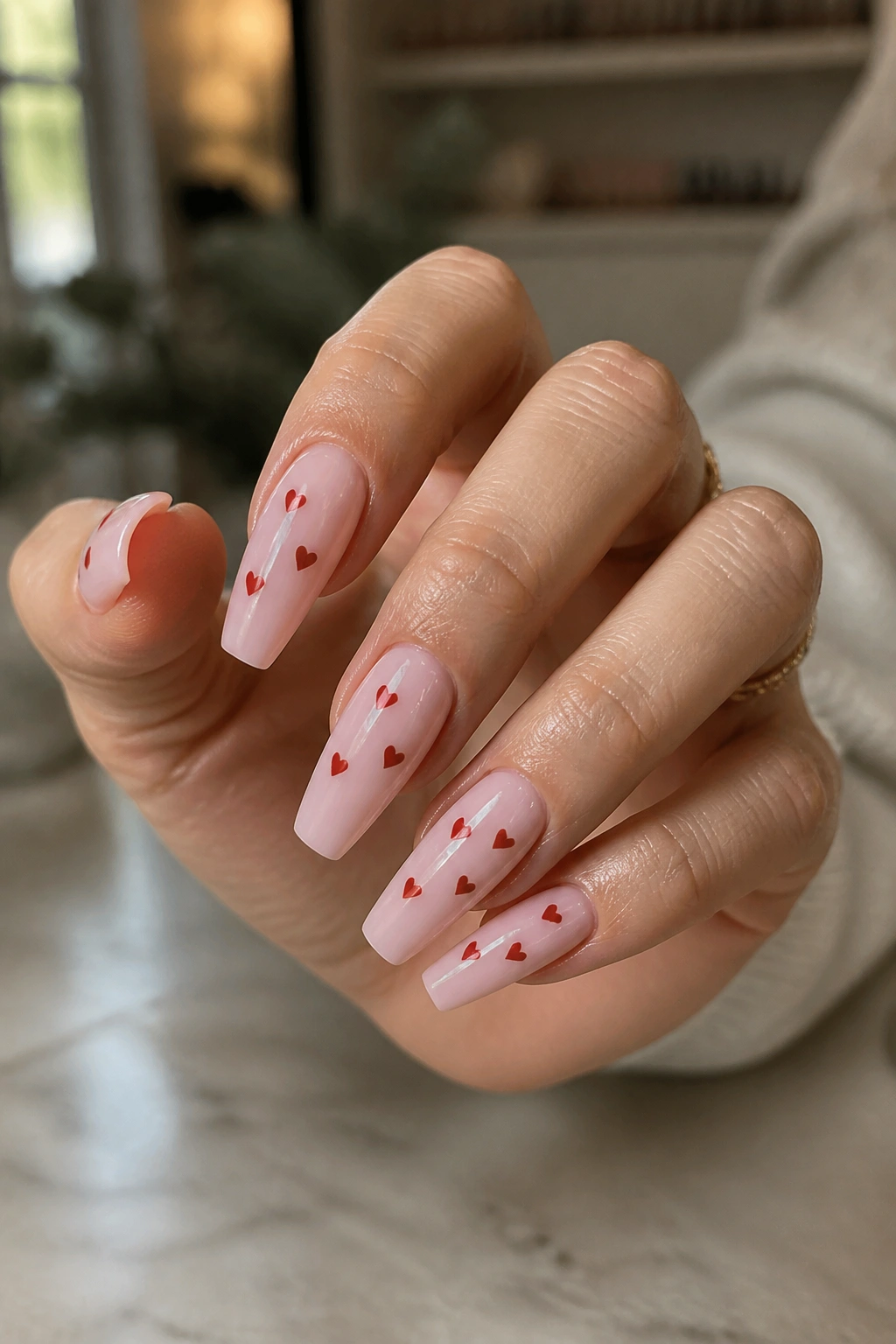 Close-up of a hand with heart-themed coffin nails on tapered tips in a salon.