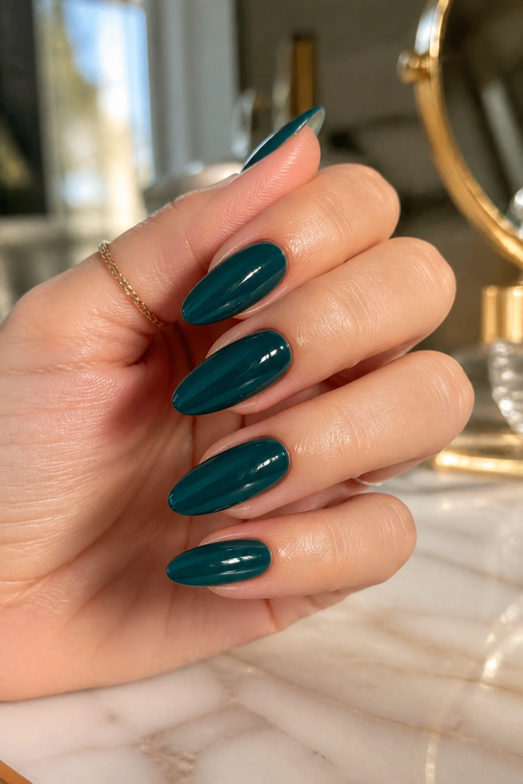 Close-up of almond nails painted deep teal with a glossy finish