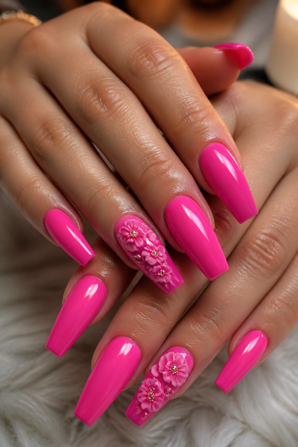 Close-up of real hands with hot pink coffin nails featuring 3D flowers on an accent nail in a warm salon setting
