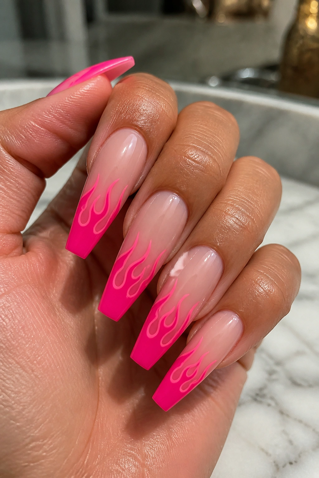 Close-up of coffin nails with hot pink flame tips on a sheer nude base on a real hand