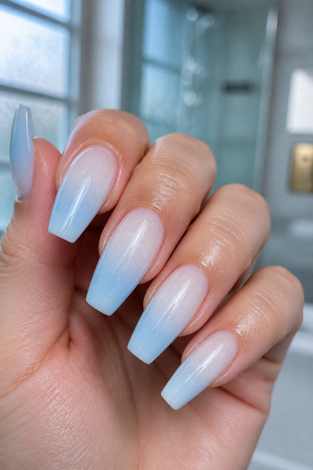 Close-up of milky white to baby blue coffin nails on a real hand with cool lighting