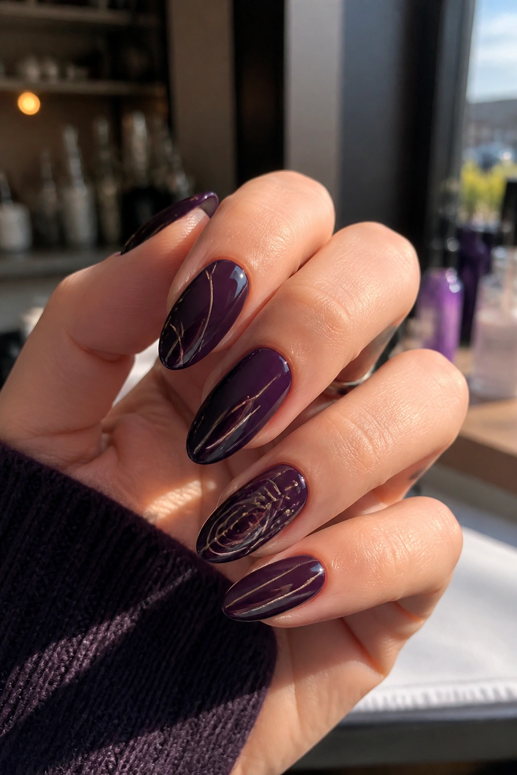 Close-up of ink-plum almond nails with abstract line art on a real hand, glossy moody manicure.
