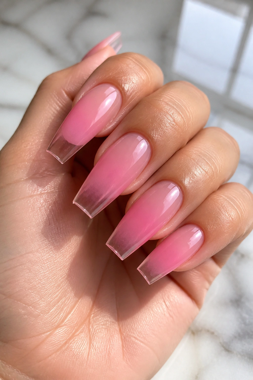 Close-up of jelly pink ombre coffin nails with translucent glassy tips on a real hand