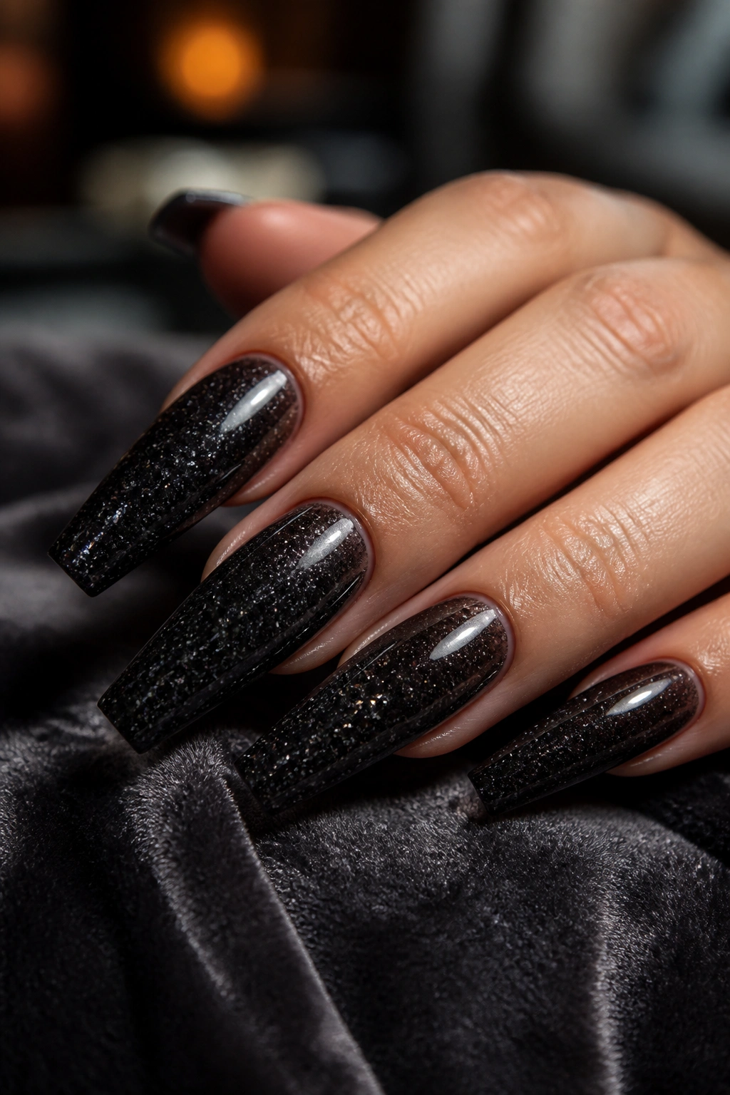 Close-up of jelly black coffin nails with suspended micro-glitter on a real hand, moody lighting