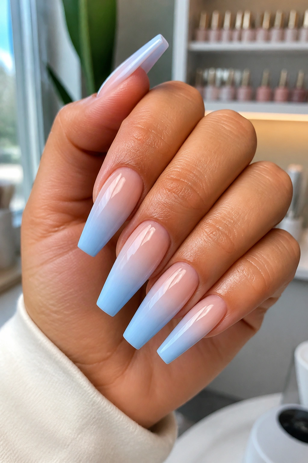 Close-up of a real hand showing light blue ombré coffin nails with a pale nude base fading to blue