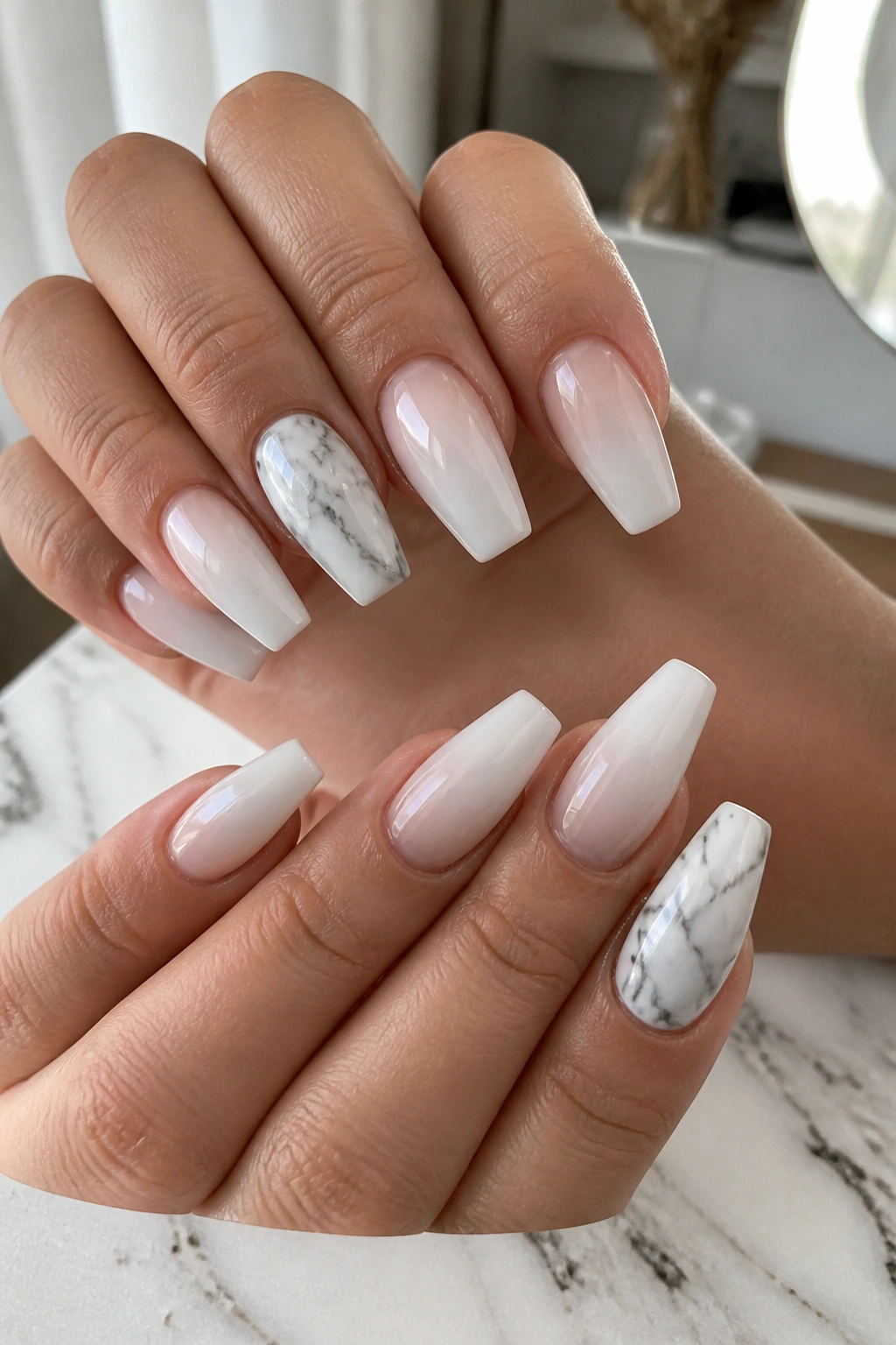 Close-up of hands showing white ombre coffin nails with marble accents on ring finger and thumb