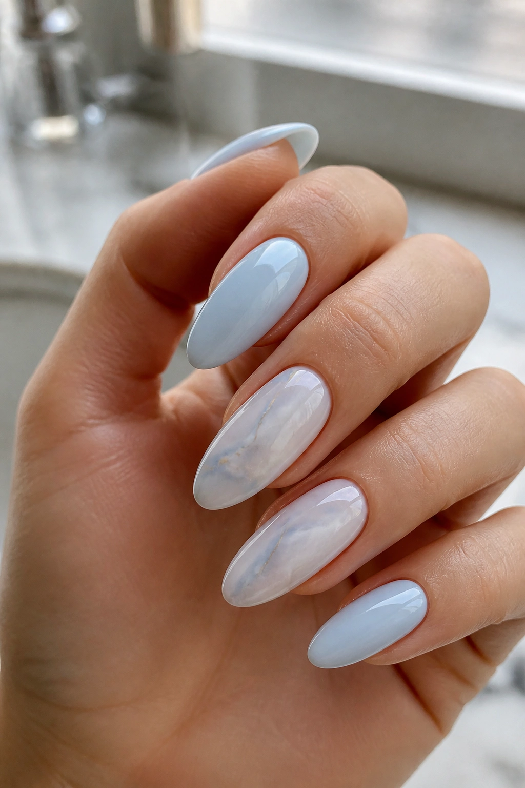 Close-up of almond nails with light blue marble design on a real hand