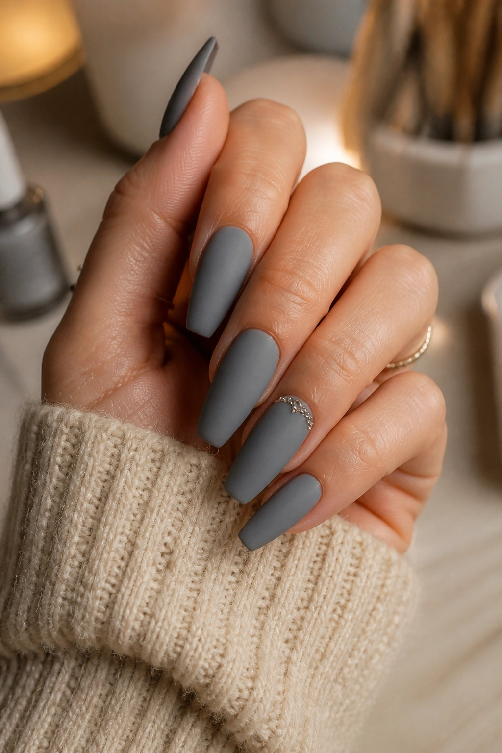 Close-up of matte ash grey nails with small crystals at the cuticle.