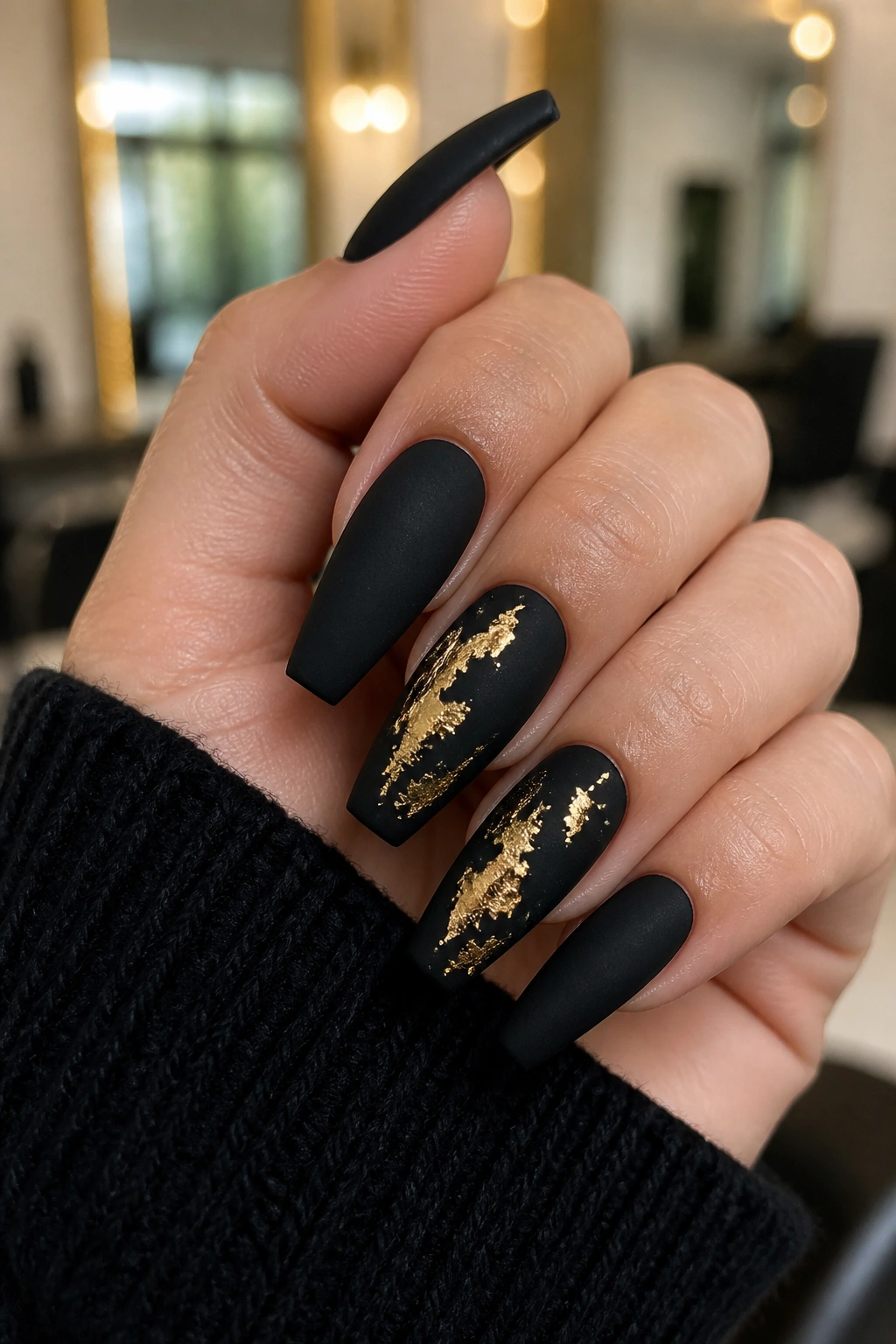 Matte black coffin nails with torn gold foil patches on real hand