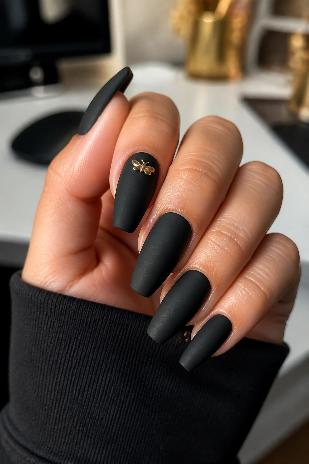 Close-up of matte black coffin nails with a single gold charm on a real hand