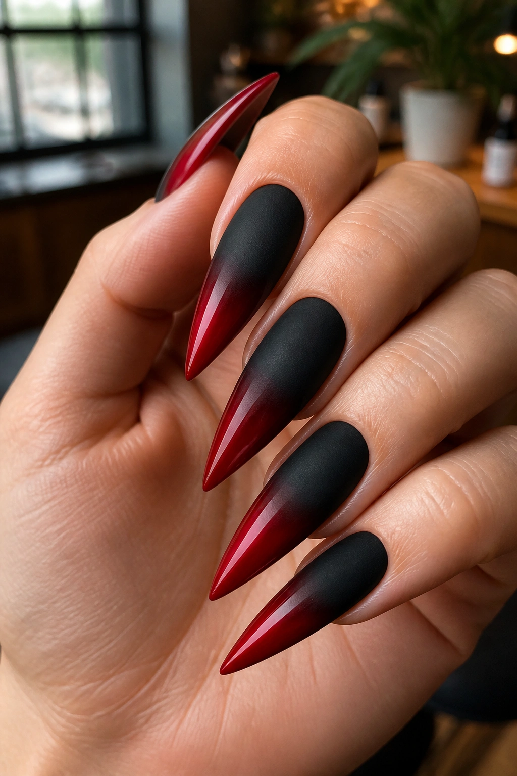 Close-up of hand with matte black to glossy red stiletto nails in a salon.