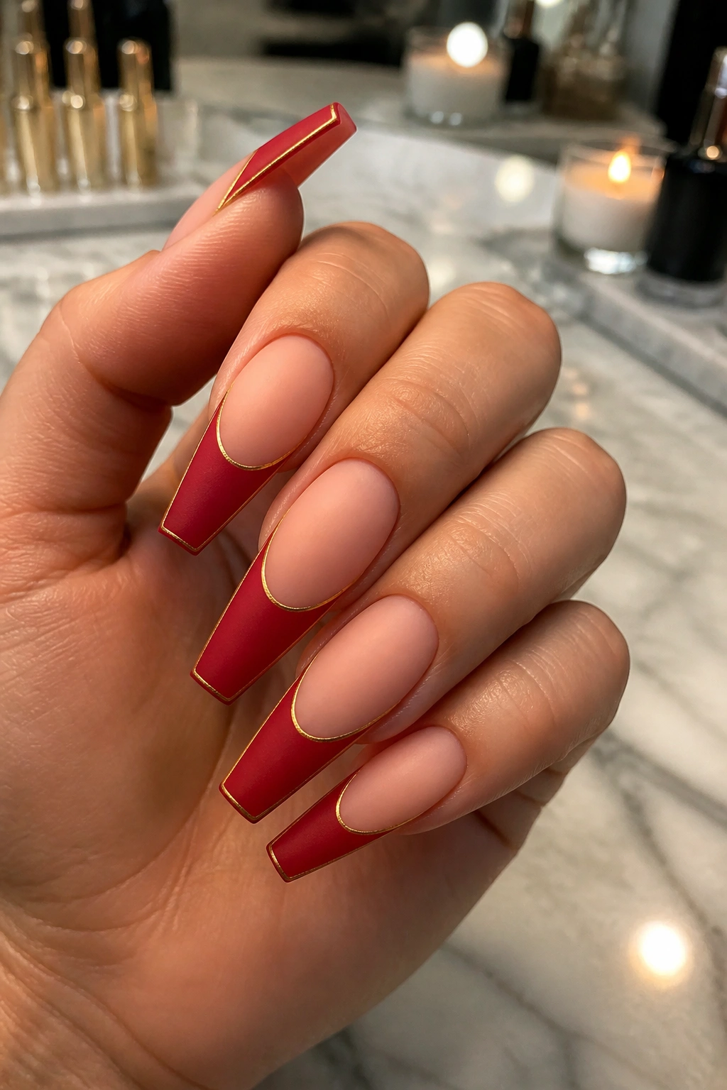Close-up of coffin nails with matte crimson tips and a thin gold outline on a real hand