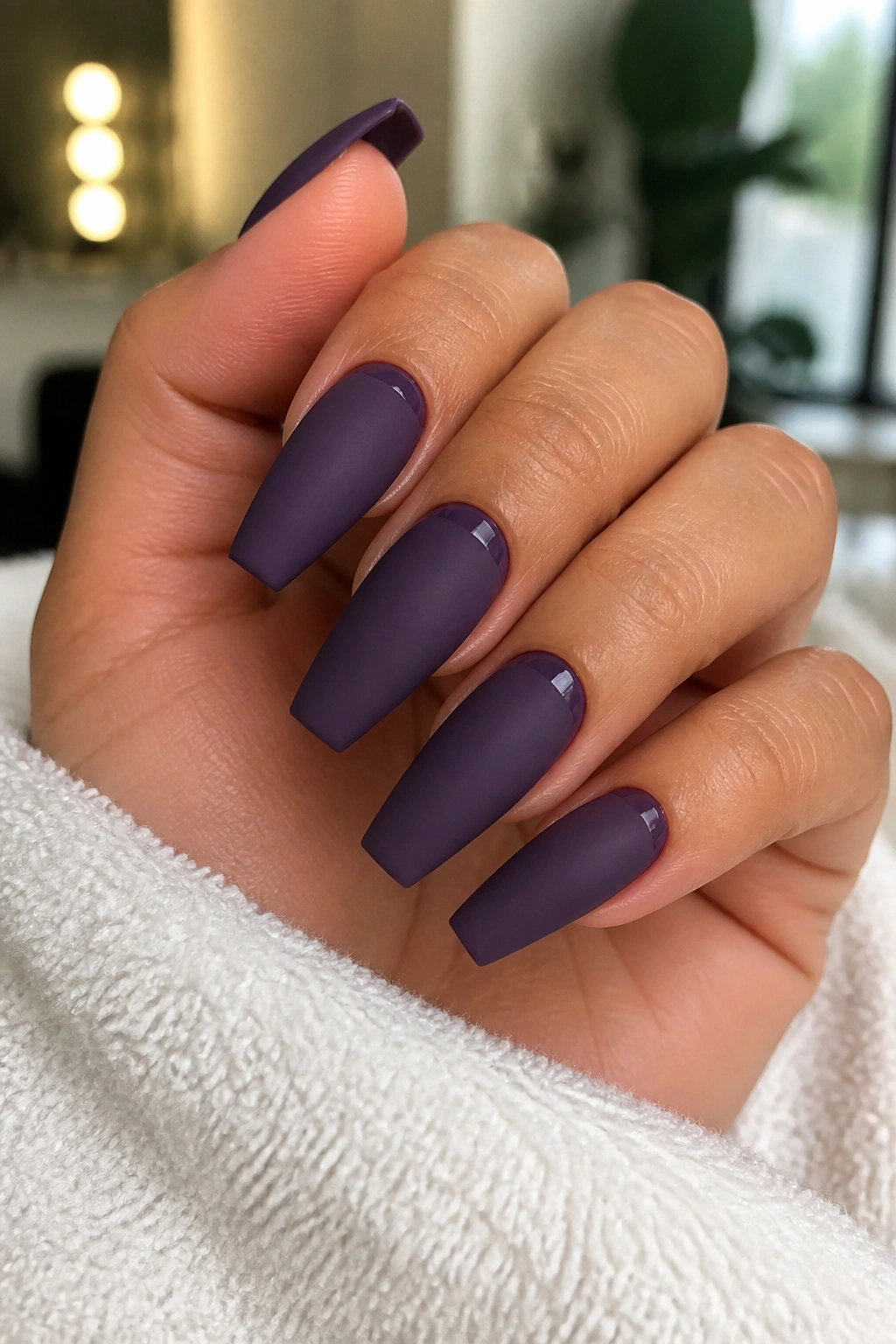 Close-up of matte grape coffin nails with glossy cuticle halos on a hand