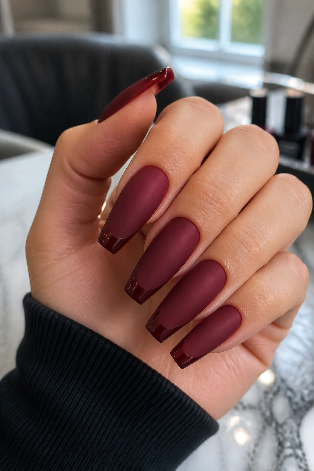 Close-up of matte maroon coffin nails with slim glossy French tips on a real hand