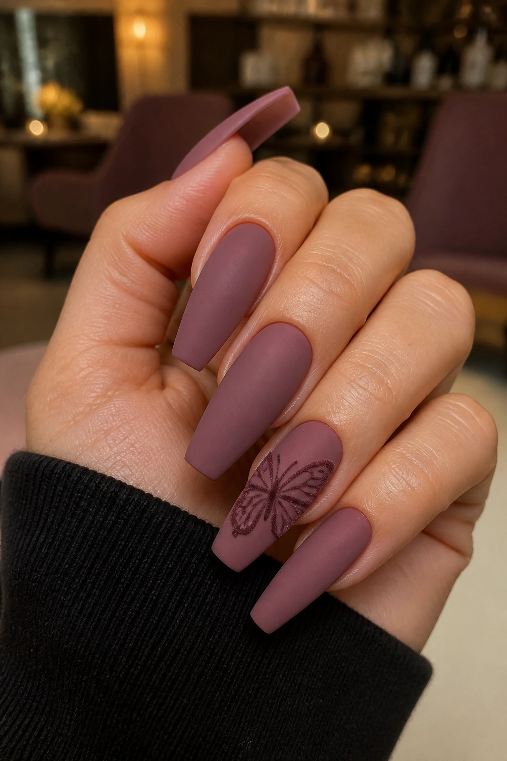 Close-up of matte mauve coffin nails with velvet butterfly accent on a real hand