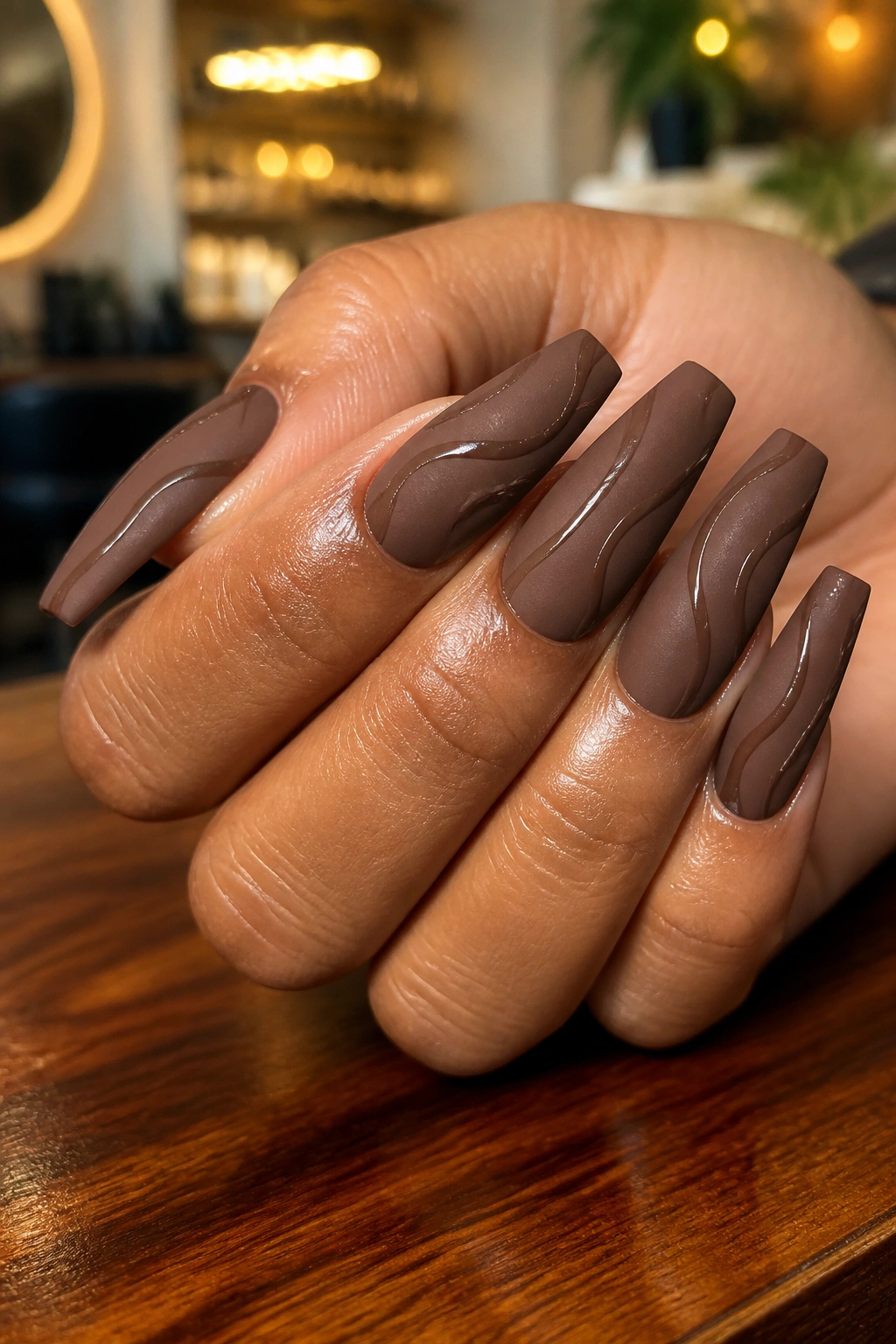 Matte mocha coffin nails with glossy swirls on a real hand