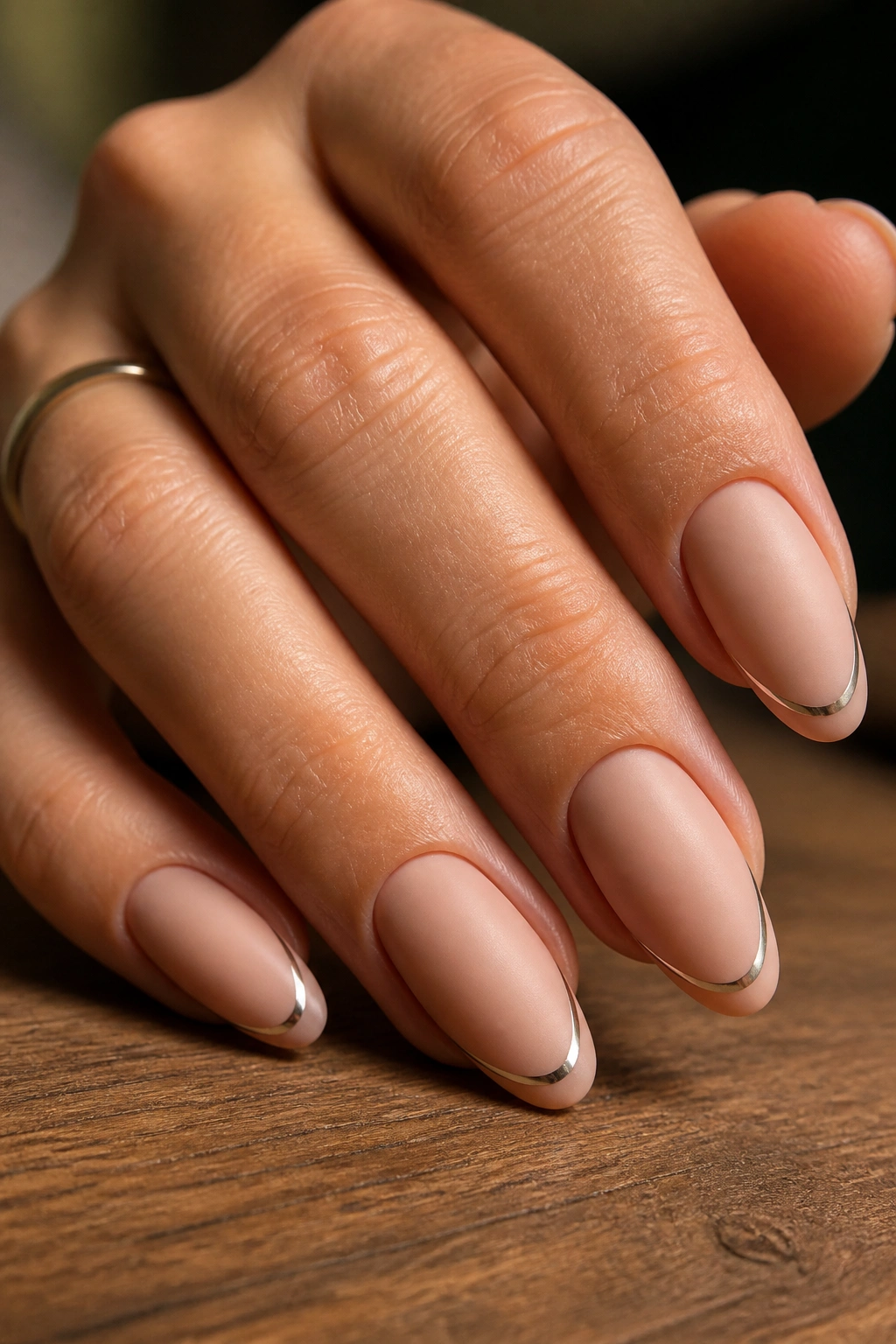 Close-up of almond nails with matte nude base and thin chrome smile line.