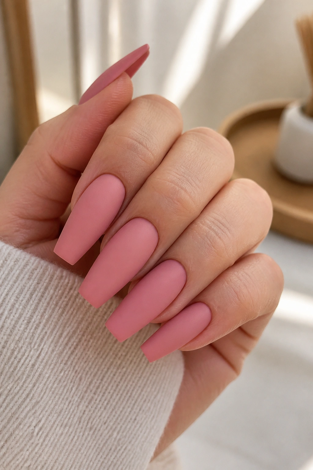 Close-up of matte rose pink coffin nails on a real hand