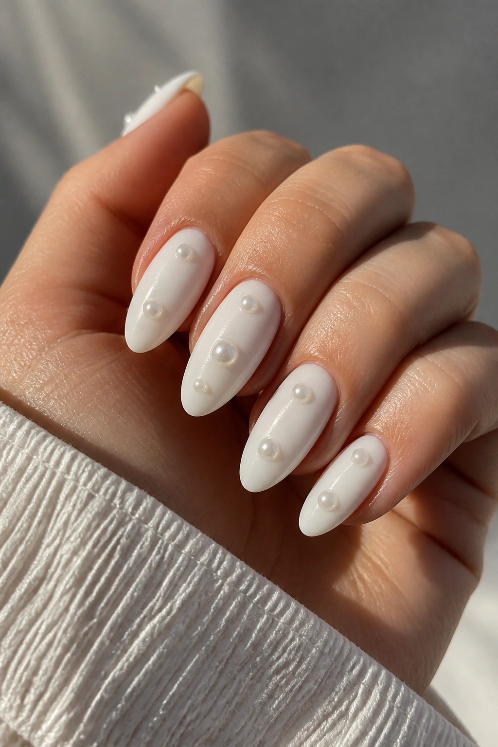 Close-up of matte white almond nails with glossy pearl drops on a real hand.