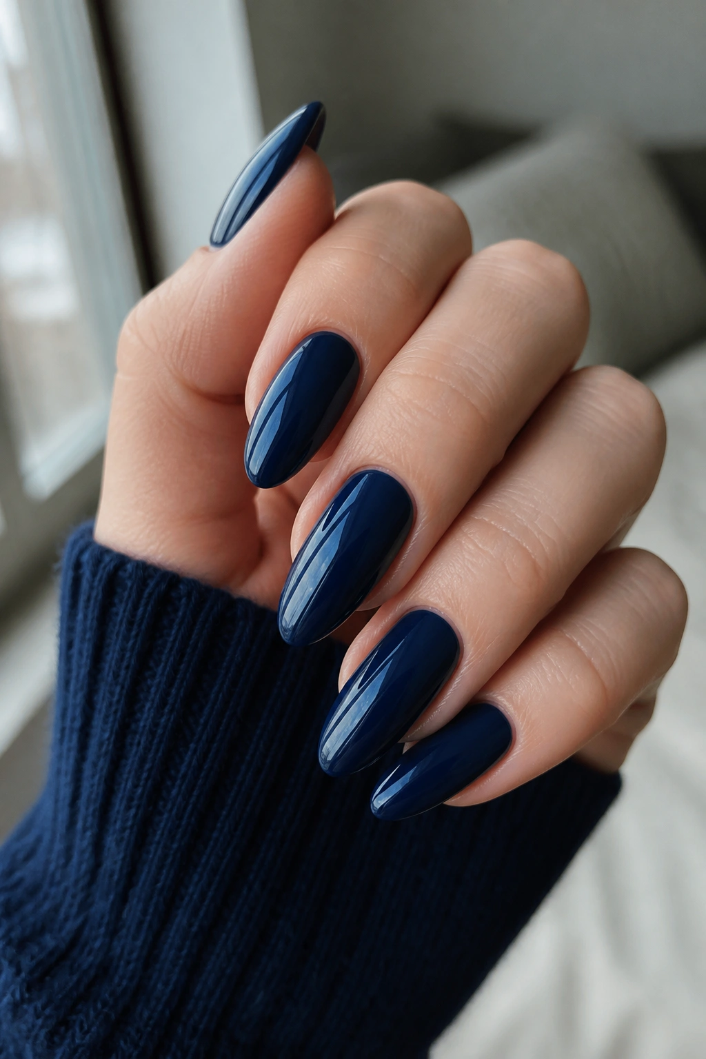 Close-up of long almond nails in midnight navy with a glossy finish on a real hand.