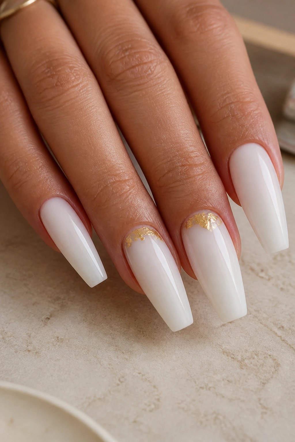 Close-up of milky white coffin nails with cuticle gold foil on a real hand at a manicure desk