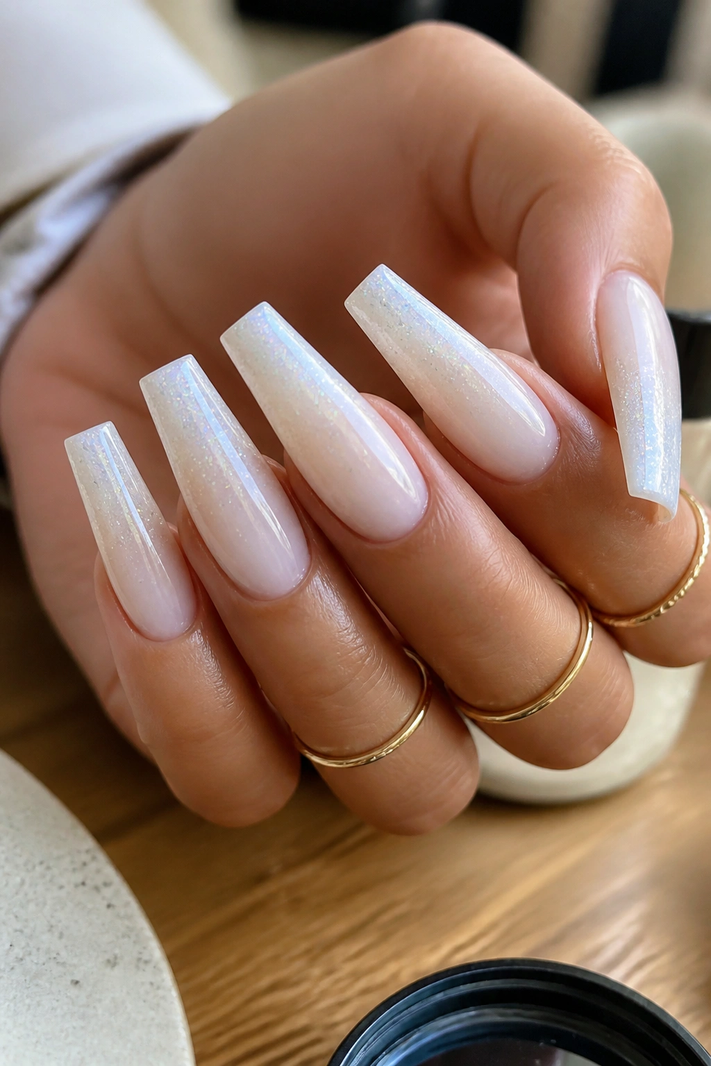 Close-up of milky white coffin nails with micro glitter fade on a real hand