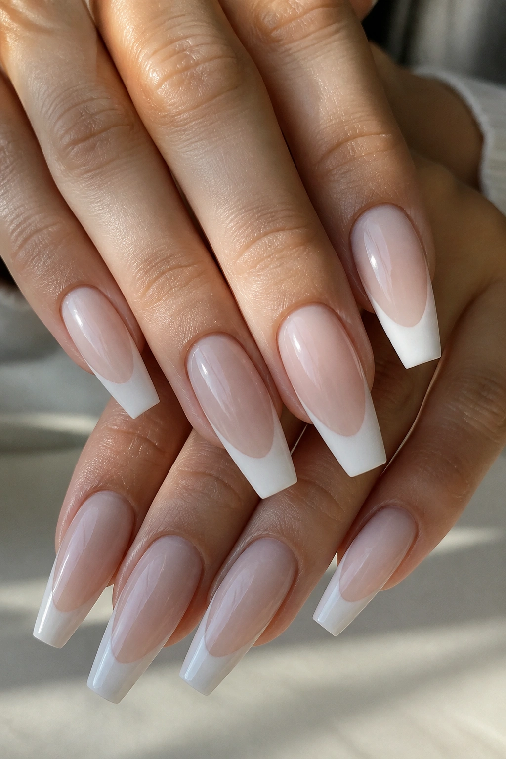 Close-up of hands with milky nude base and deep smile lines on coffin nails.