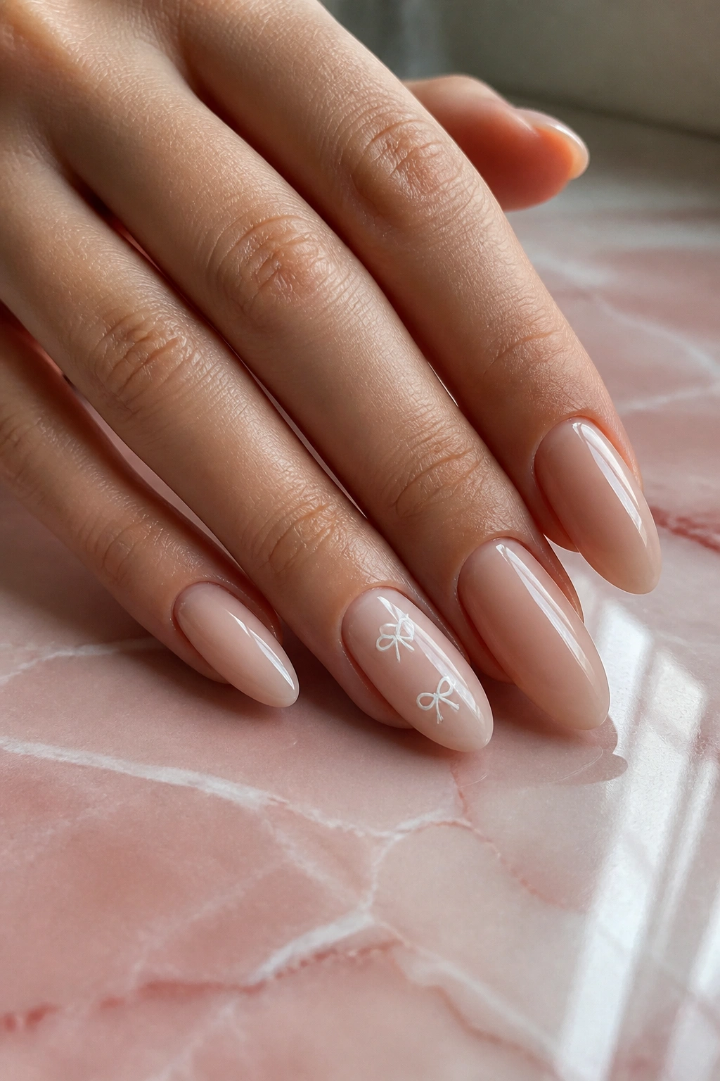 Close-up of milky nude almond nails with tiny white bows on accent nails