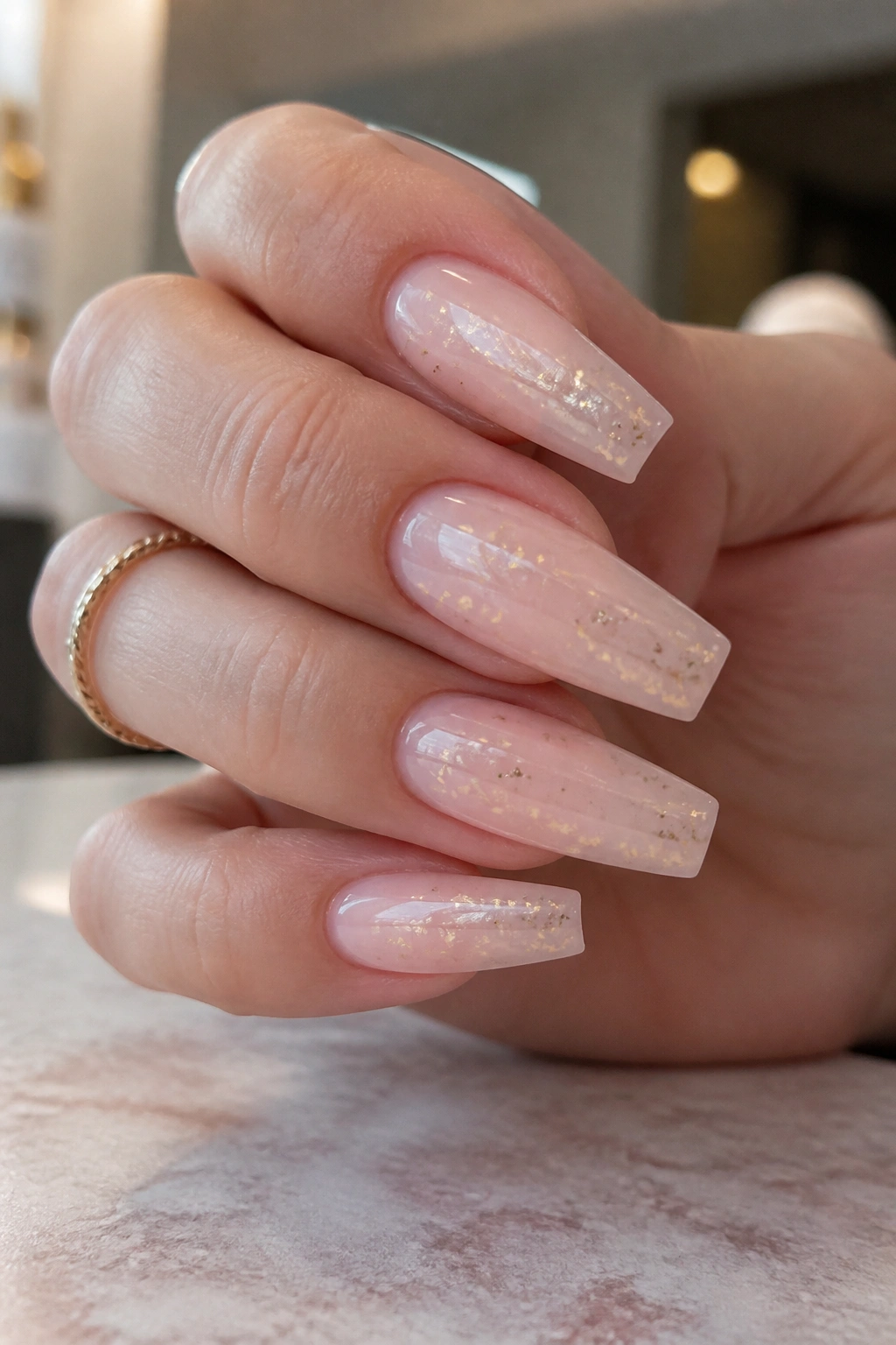 Close-up milky pink coffin nails with suspended gold flakes inside builder gel
