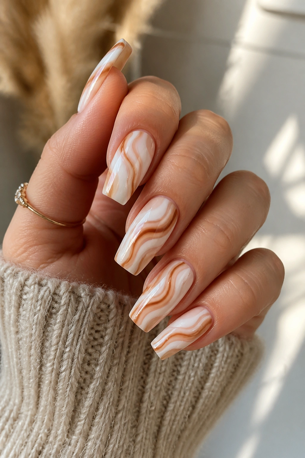 Milky white nails with caramel swirls on a real hand