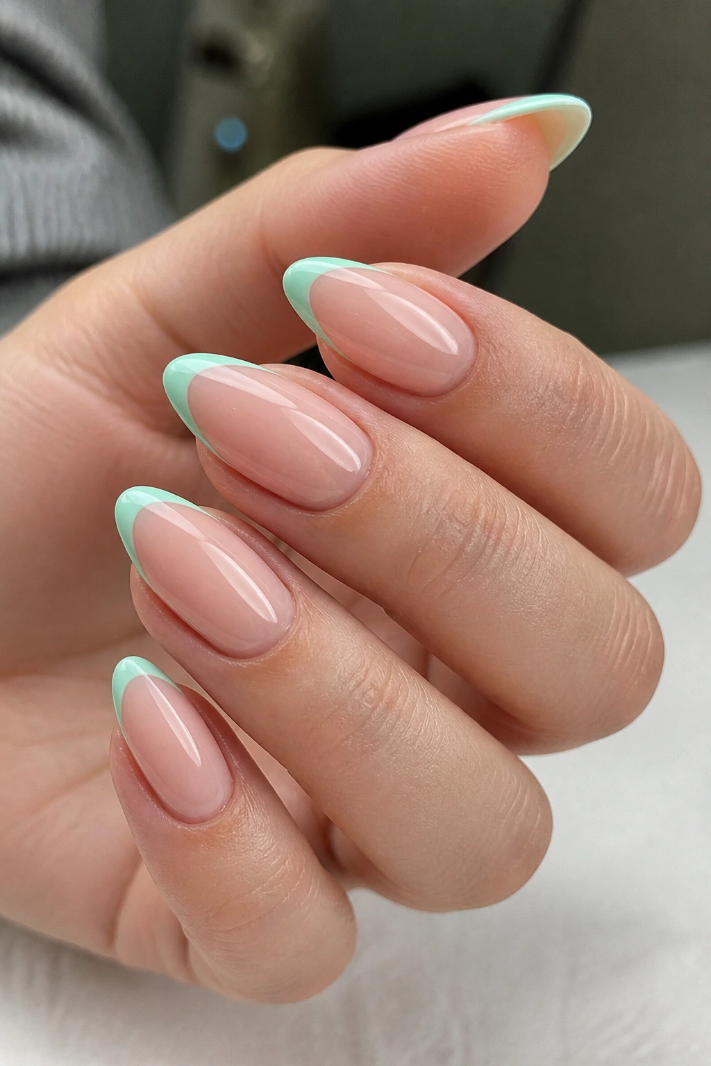 Close-up of almond nails with mint French tips on nude base