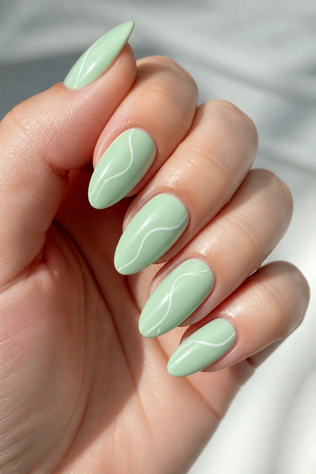 Close-up of mint and white swirl almond nails on a real hand