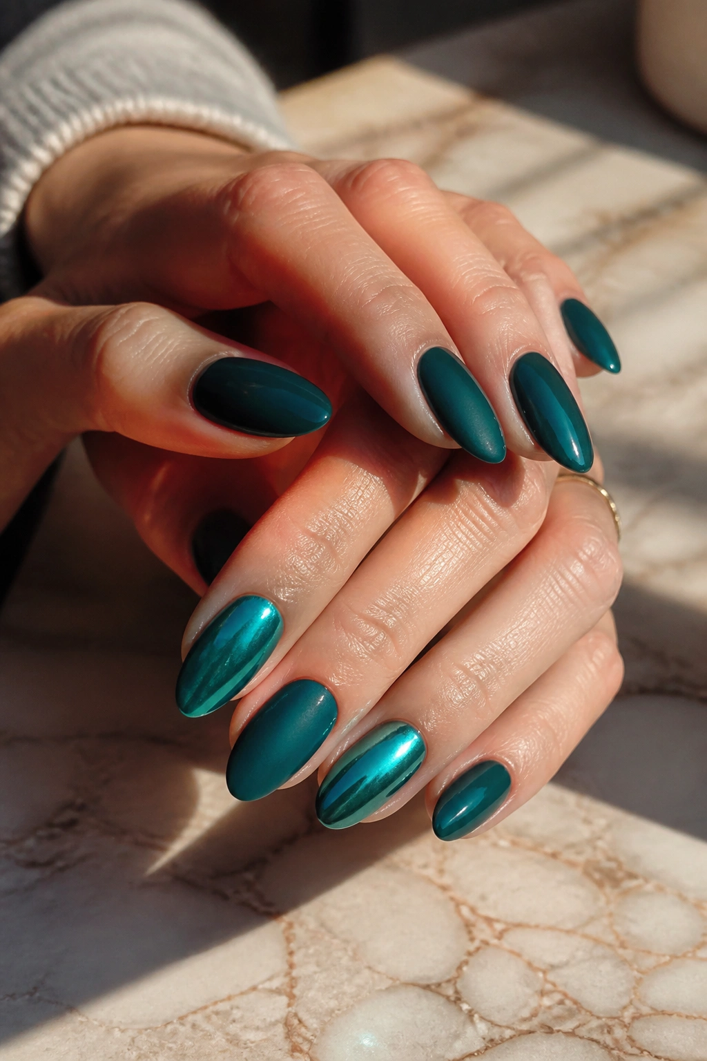 Close-up of mixed teal almond nails with one chrome accent nail on hands