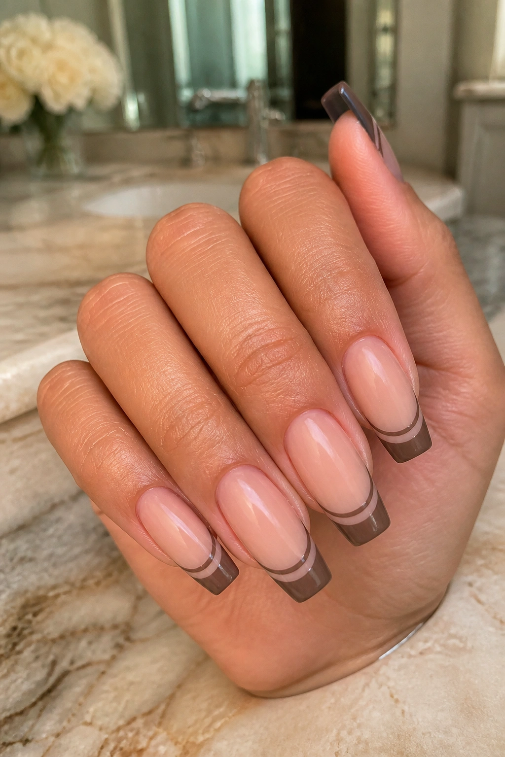 Close-up of mocha double French tips on coffin nails with precise spacing