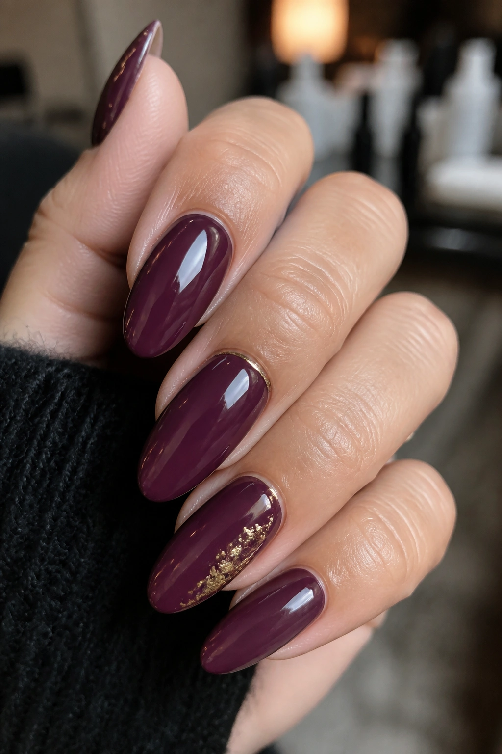 Close-up of deep mulberry almond nails with gold detail on a real hand