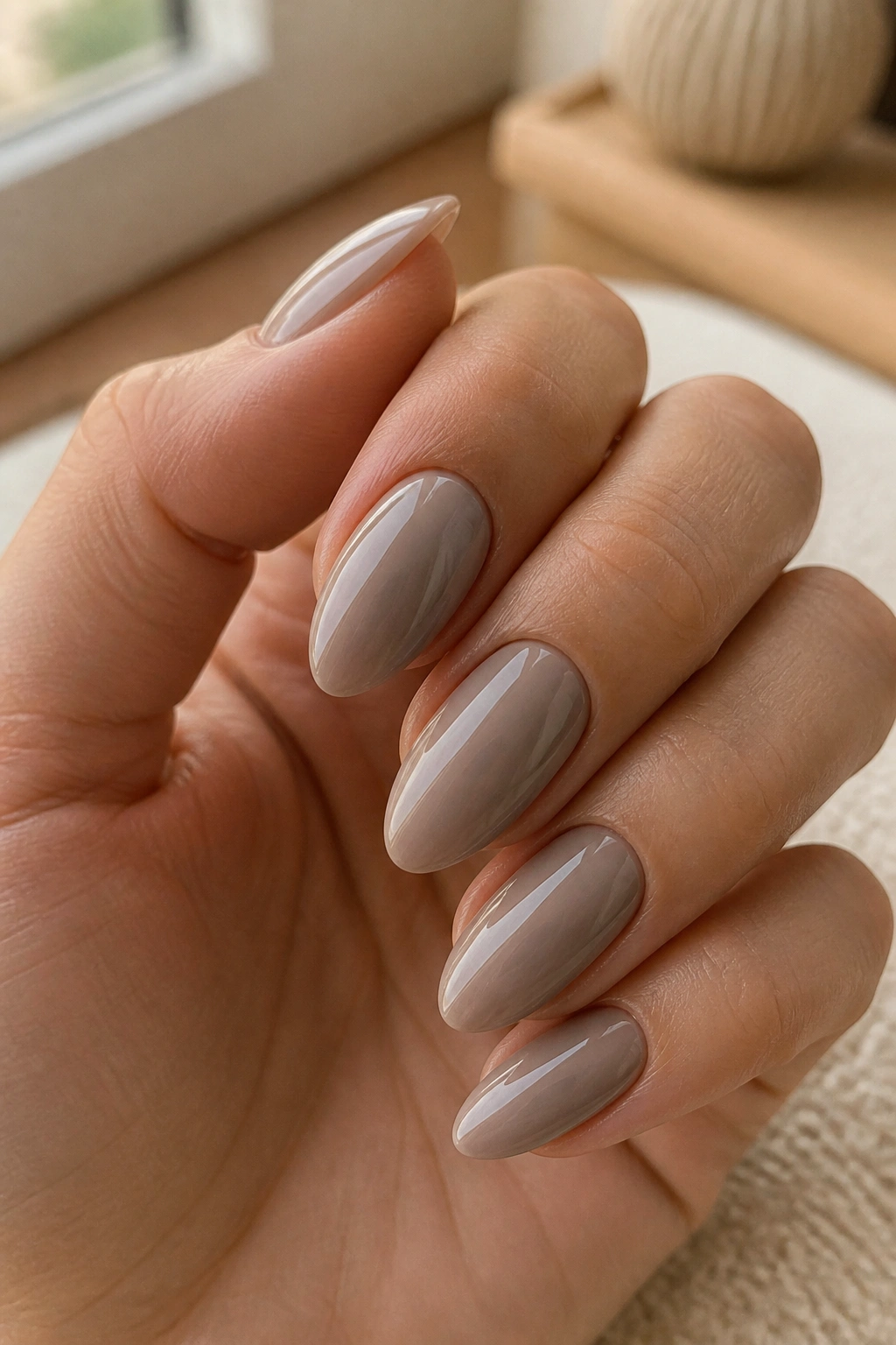 Close-up of almond nails painted in mushroom greige with glossy finish on a real hand