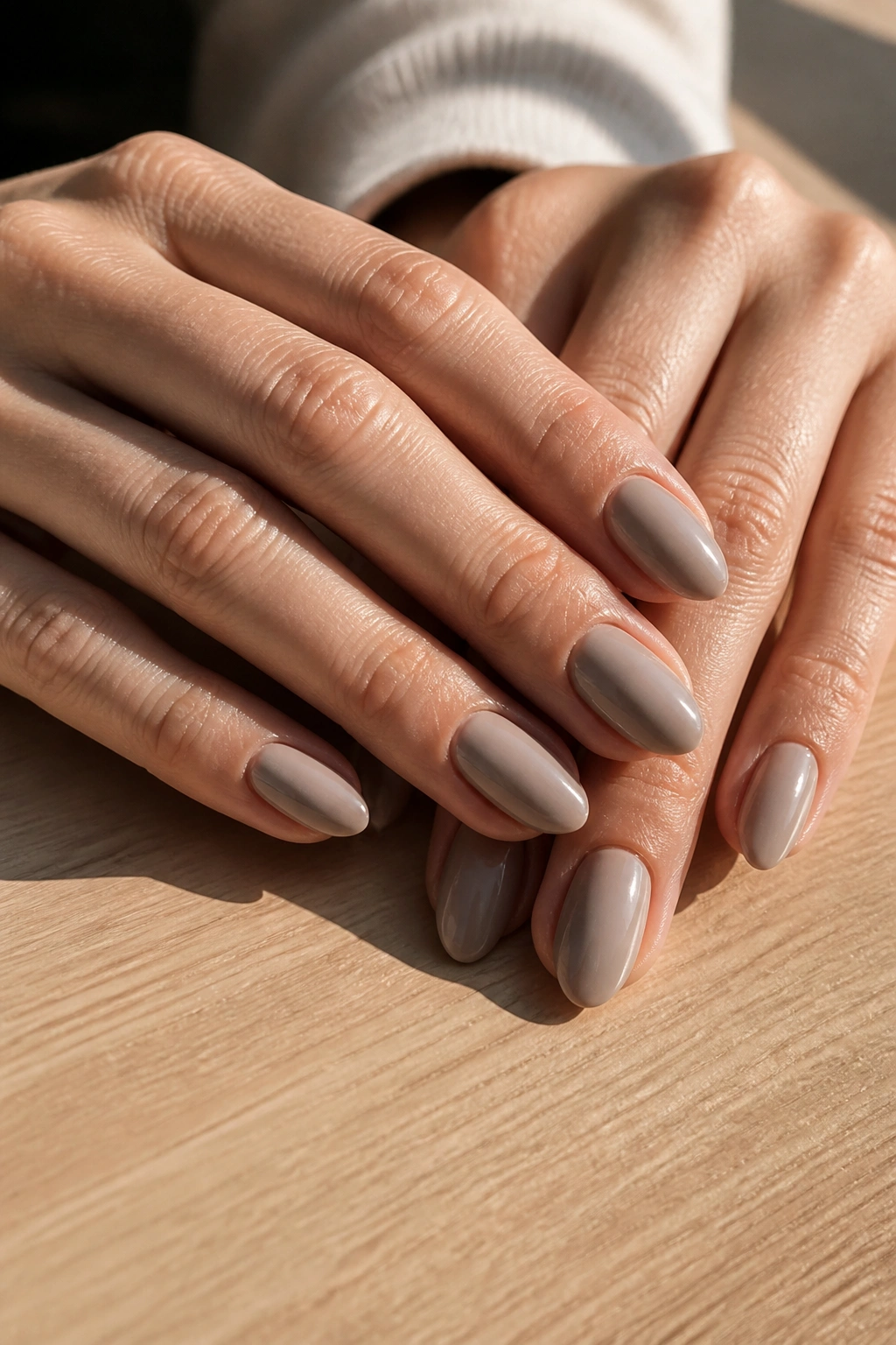 Close-up of a real hand with mushroom nude almond nails on light wood, natural daylight
