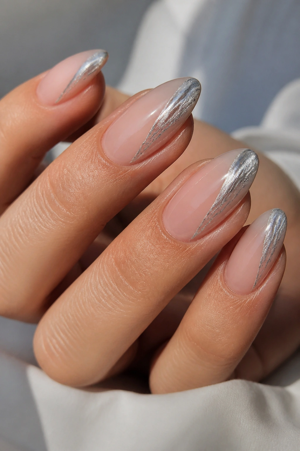 Close-up of almond nails with sheer nude base and silver abstract strokes