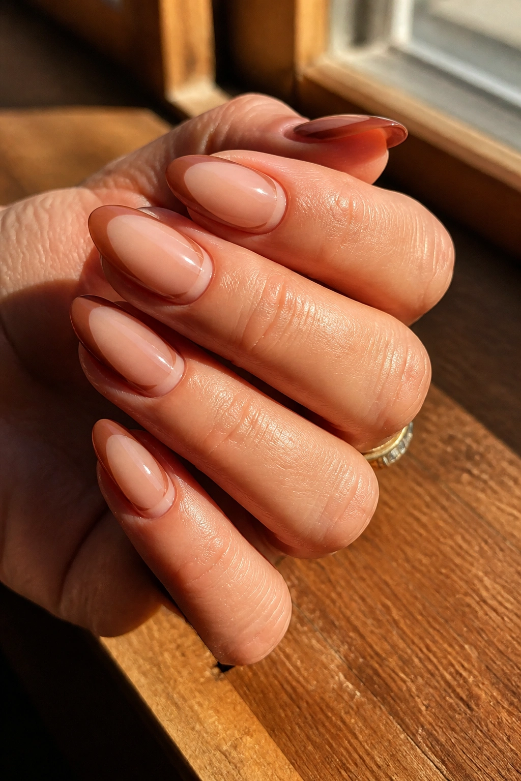 Close-up of a hand with cinnamon-brown negative-space French tips on almond nails