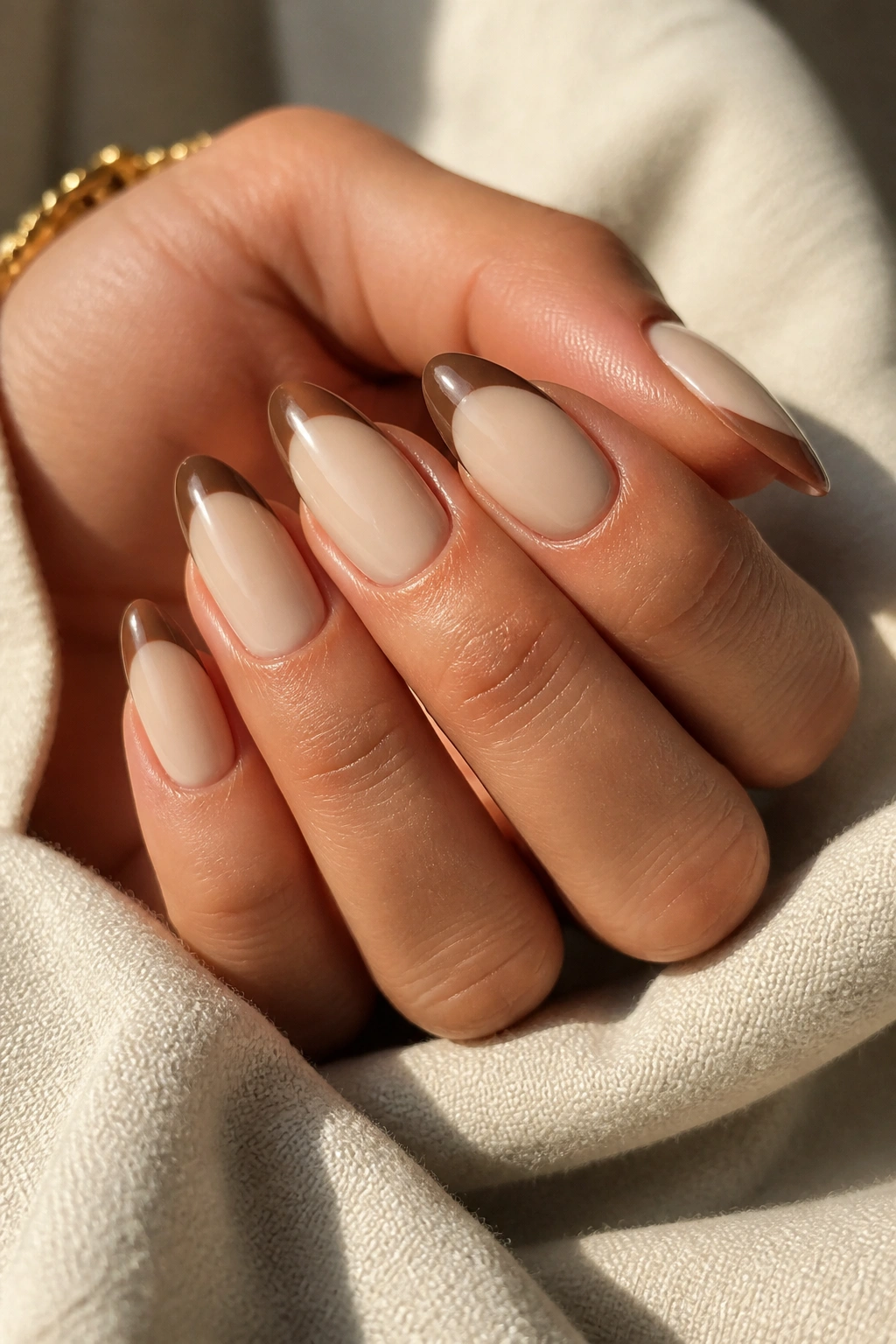 Close-up of a hand with oatmilk base and walnut brown French tips on almond nails