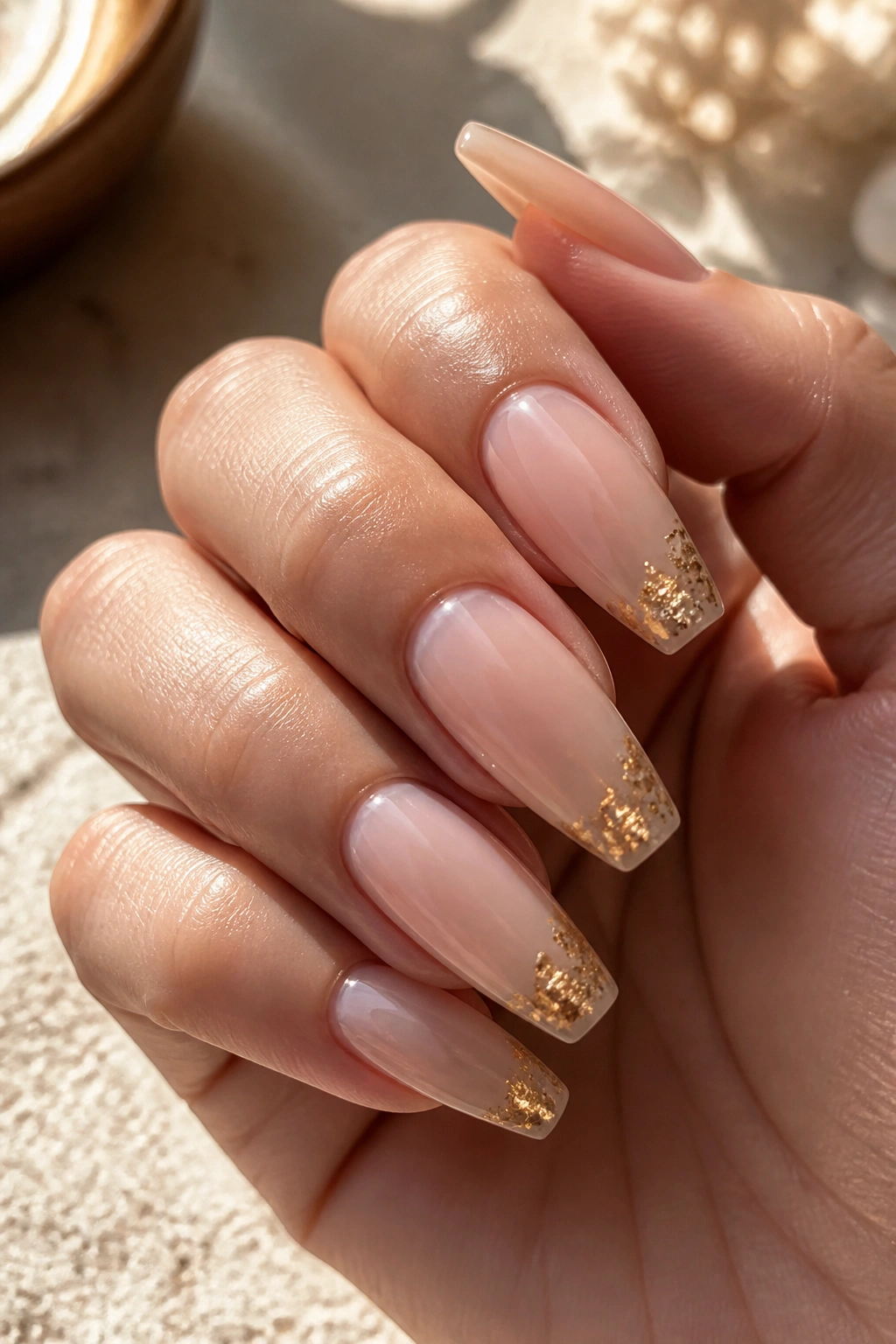 Close-up of coffin nails with sheer nude base and tiny gold foil on tips