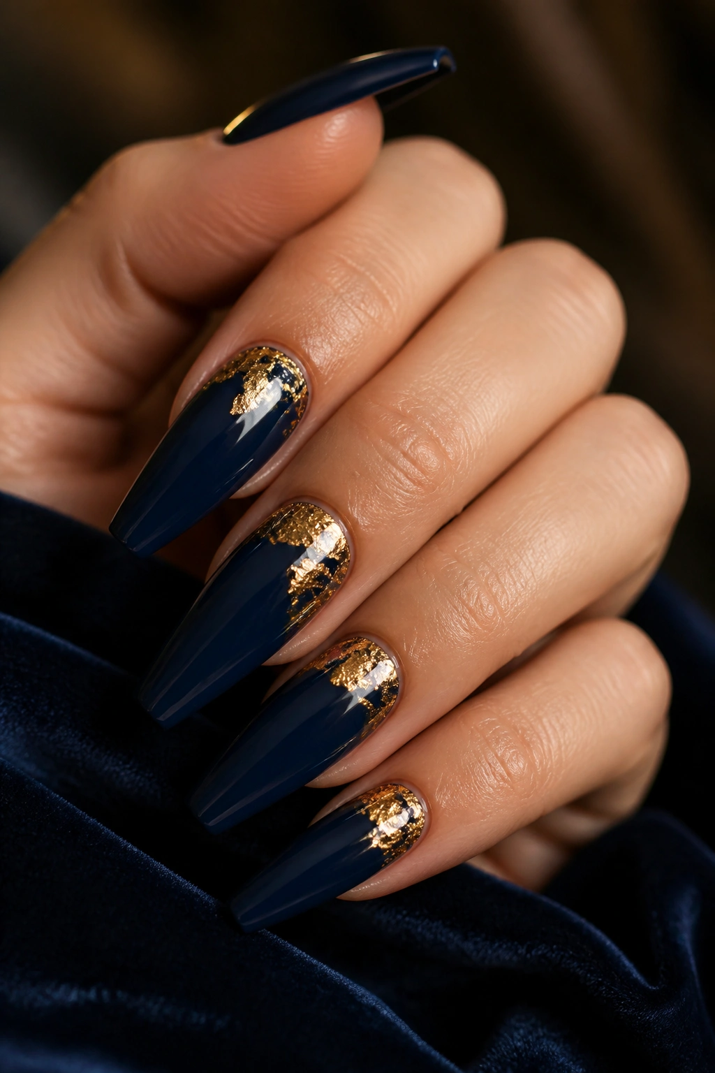 Close-up of navy coffin nails with gold foil accents on a real hand resting on dark velvet