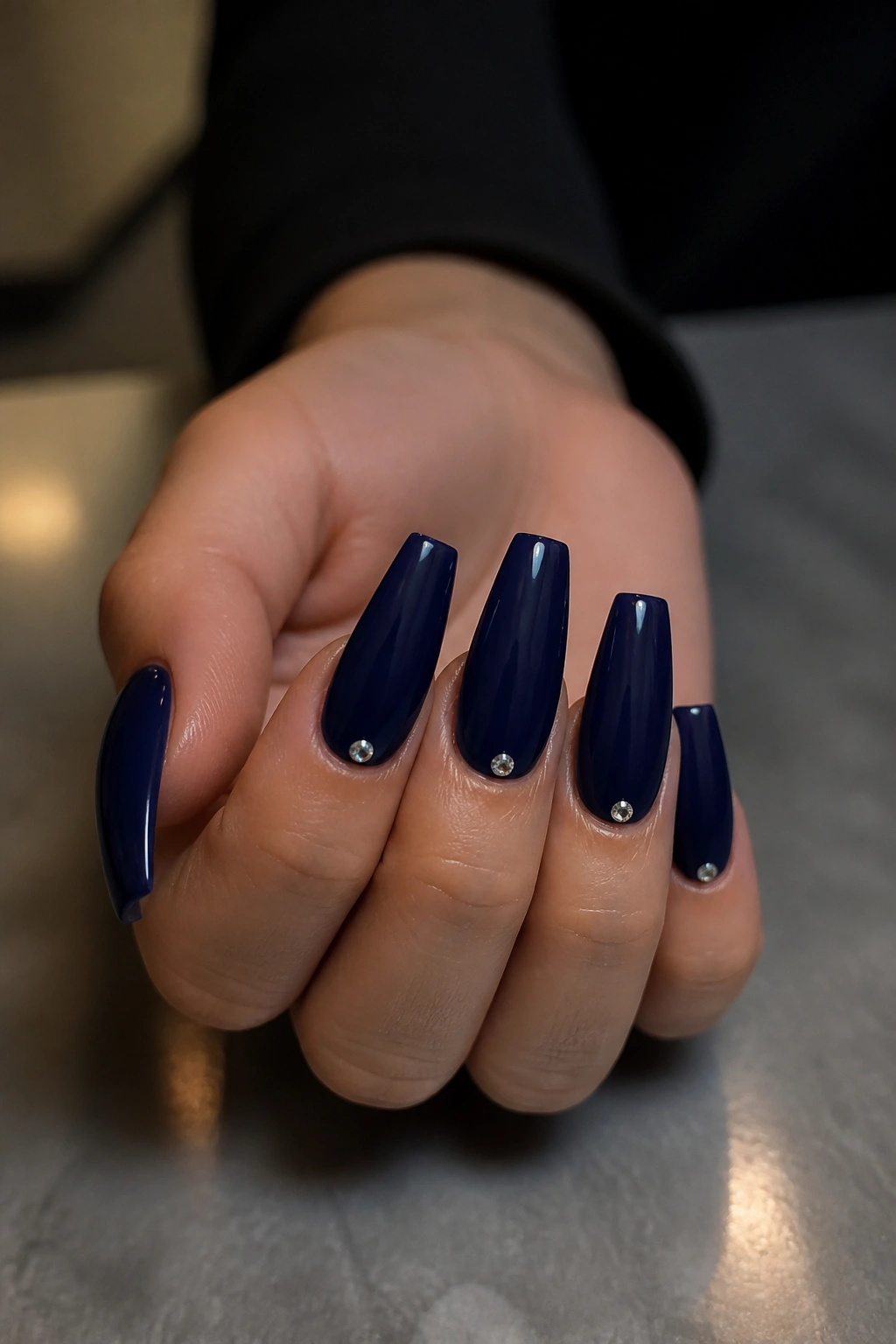 Navy coffin nails with tiny crystal accents at the cuticle on a real hand
