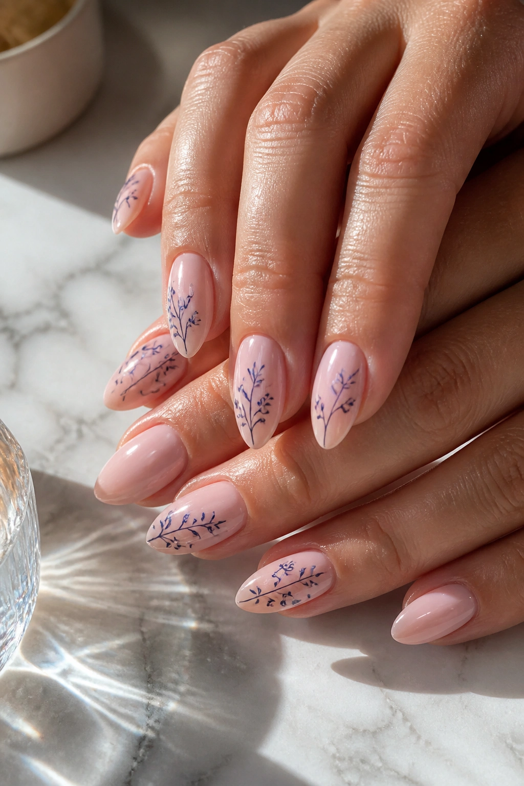 Almond nails with blush base and navy floral line art on a marble vanity