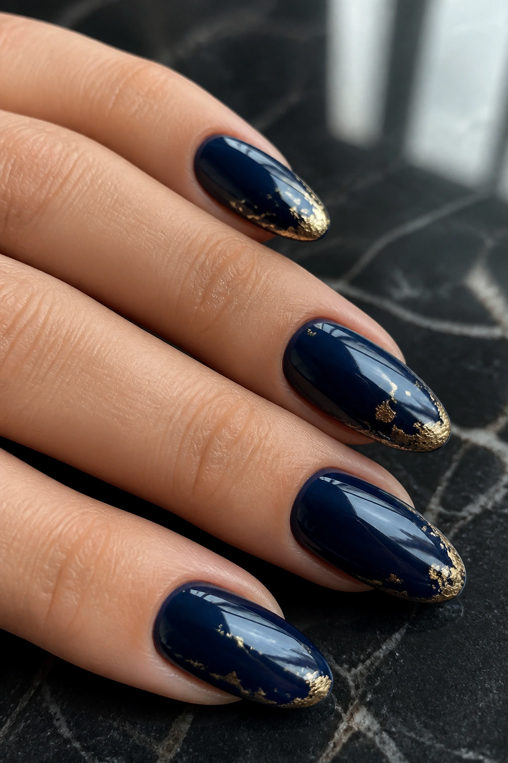 Deep navy nails with thin gold foil close-up on real hand