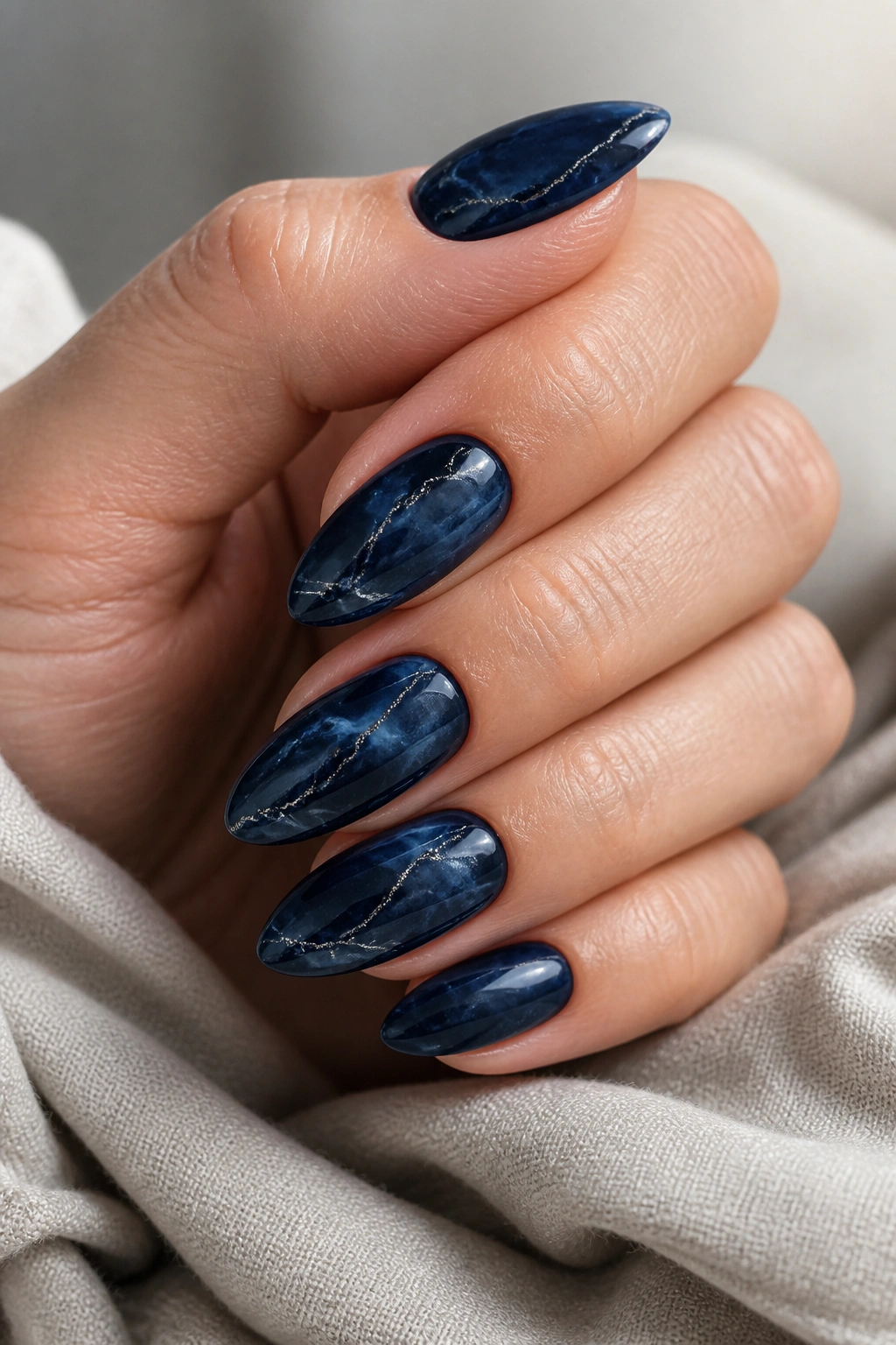 Close-up of navy almond nails with marble pattern and silver veins on a real hand