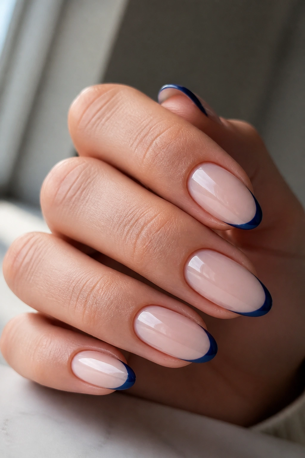 Almond nails with navy micro-French tips on milky base close-up.