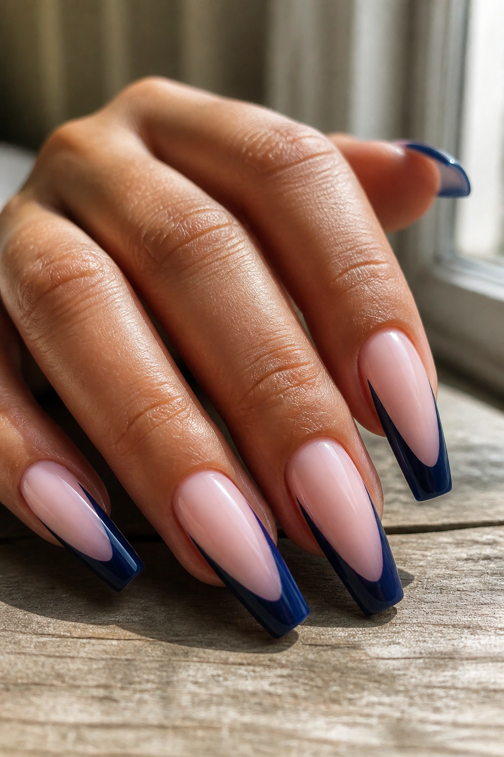 Close-up of nails with thick navy arcs over milky pink base