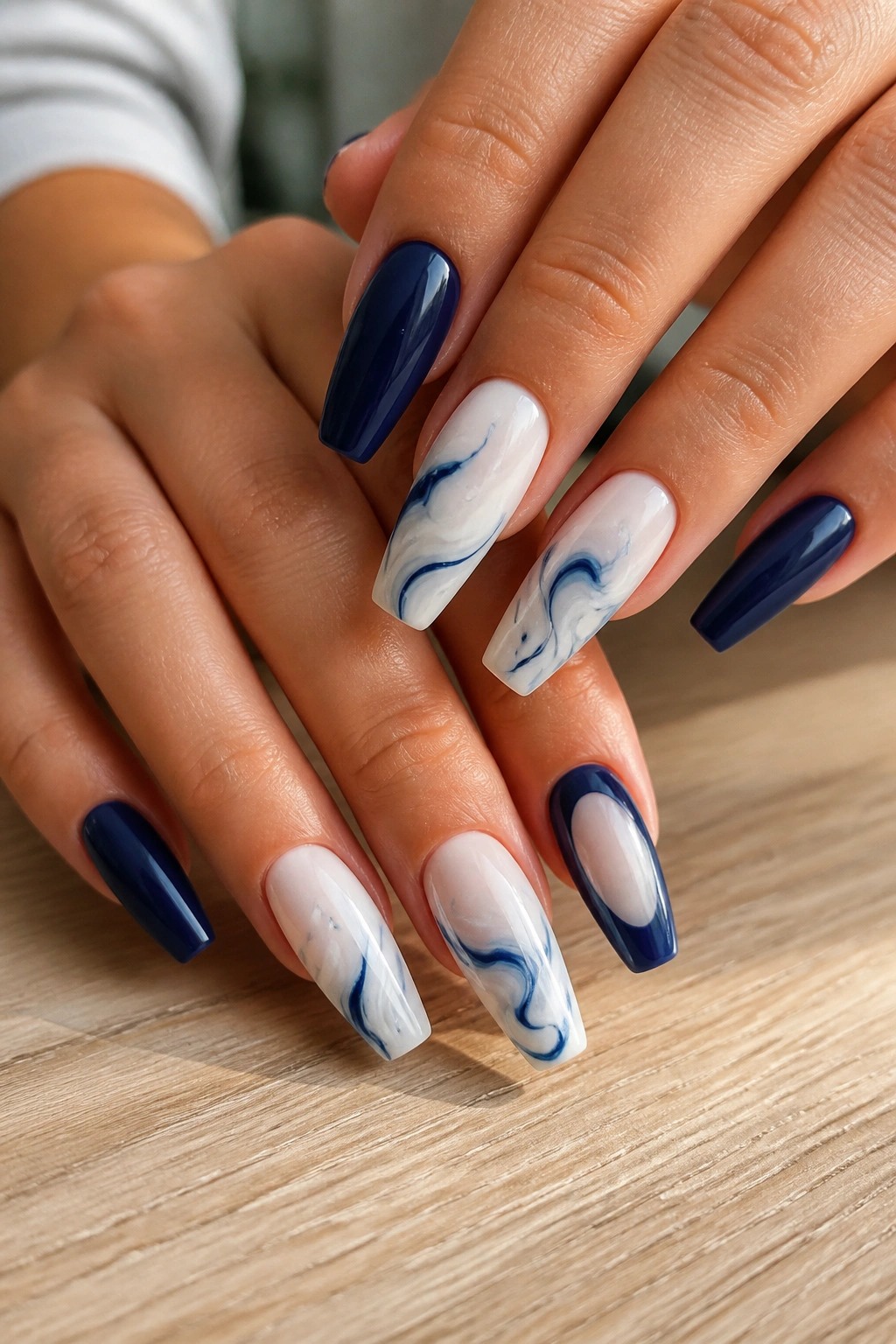 Close-up of hands with navy and white swirl coffin nails on a natural window-lit manicure table